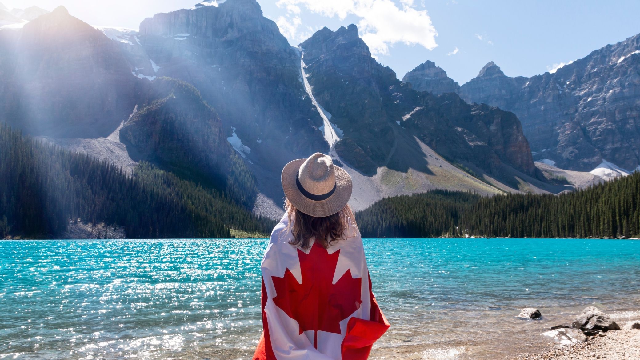 Viajera con una bandera canadiense frente al lago Moraine, en las Montañas Rocosas