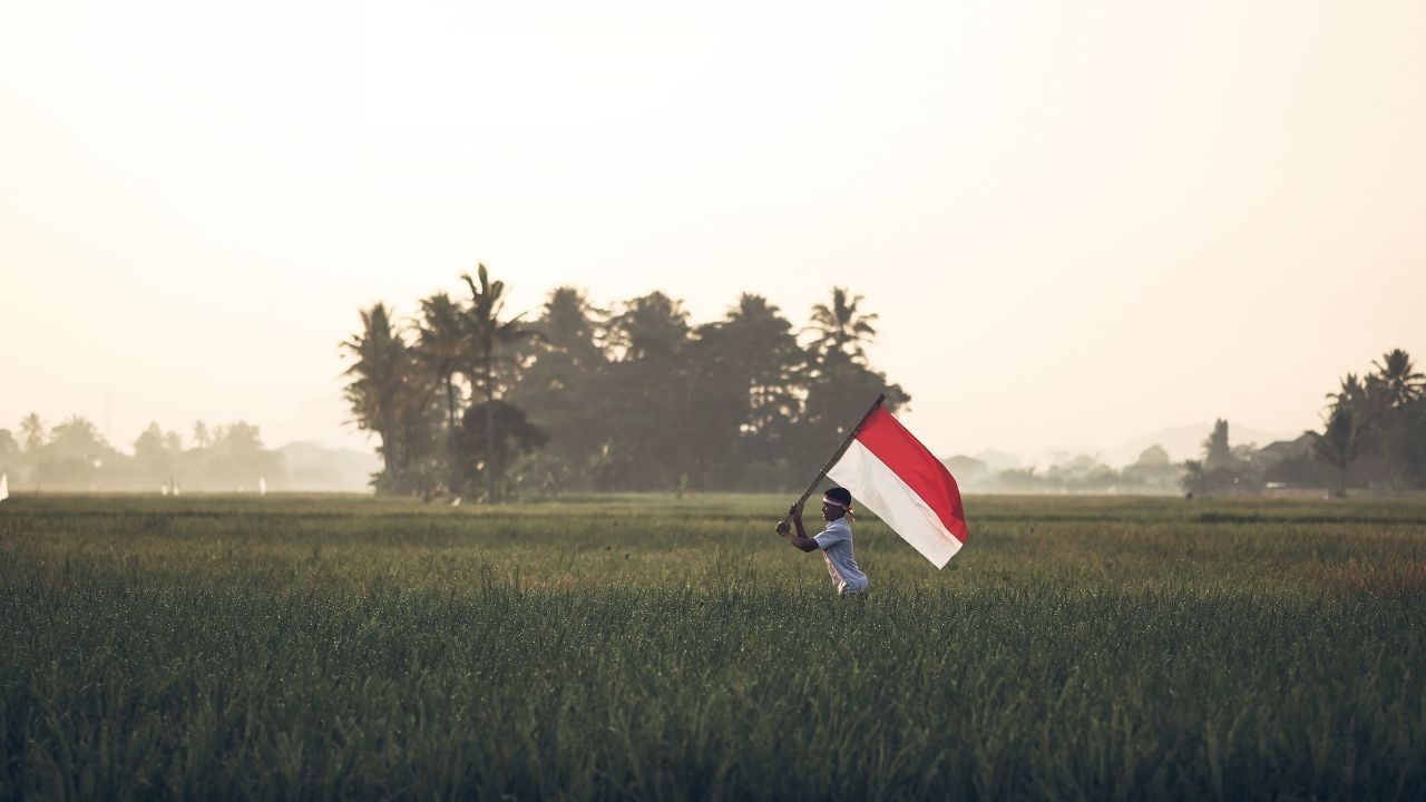 Un homme traverse une rizière en portant le drapeau indonésien au lever du soleil