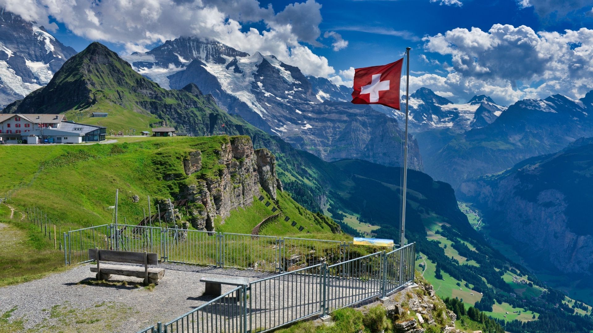 Um miradouro de montanha com a bandeira suíça face aos cumes dos Alpes berneses