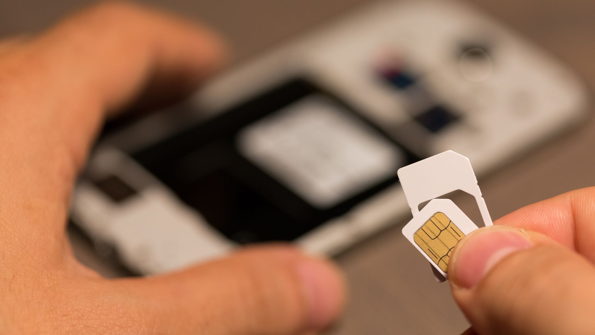 Main tenant une carte SIM nano devant un téléphone, prête à être insérée