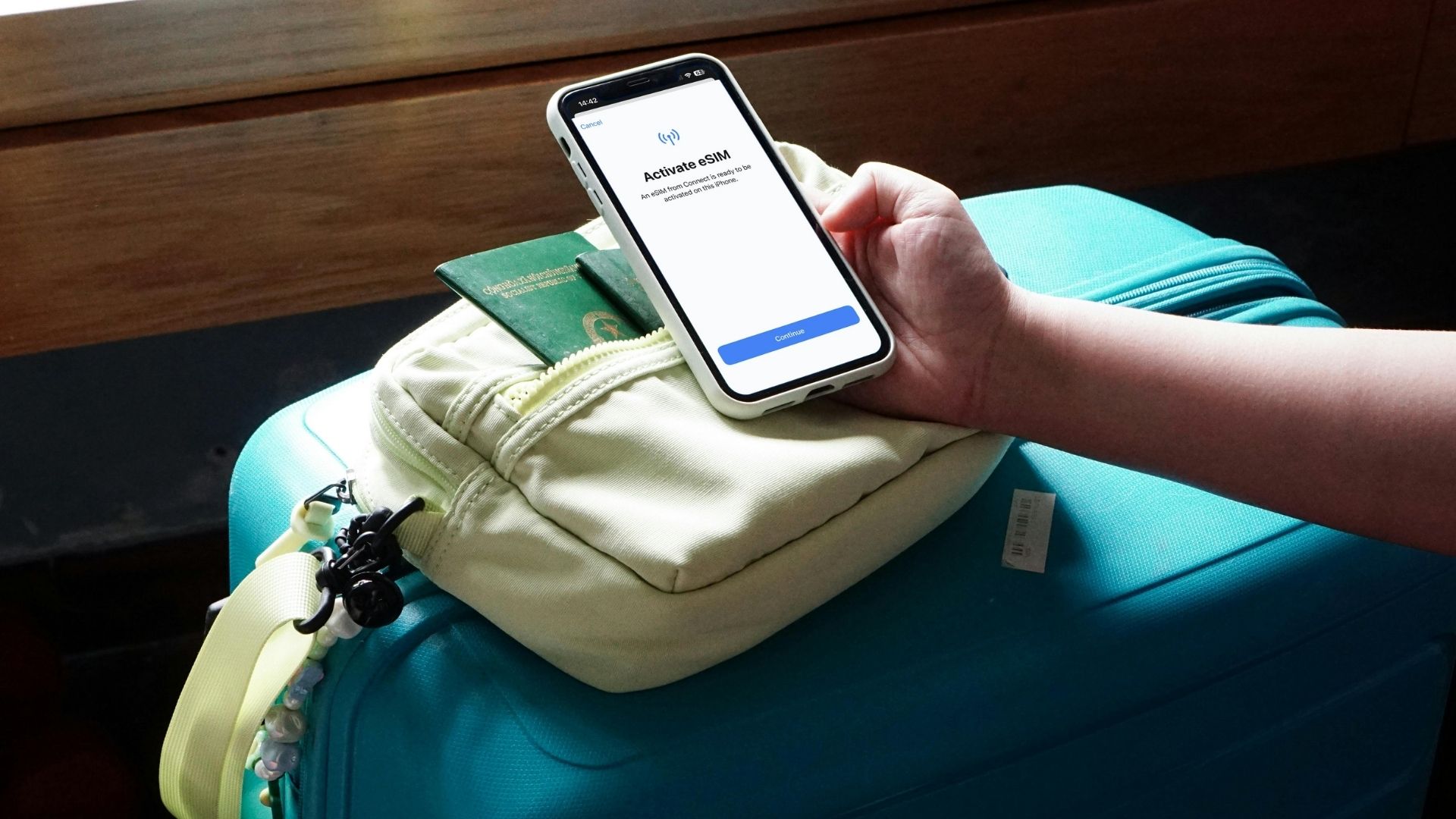 Ecrã "Ativar eSIM" num iPhone pousado sobre uma mala, com passaporte ao lado